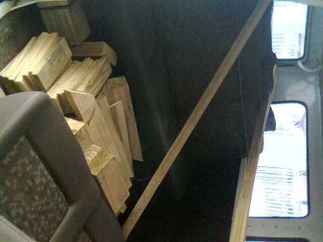 A pile of wood planks stacked inside the Kombi, next to the seats