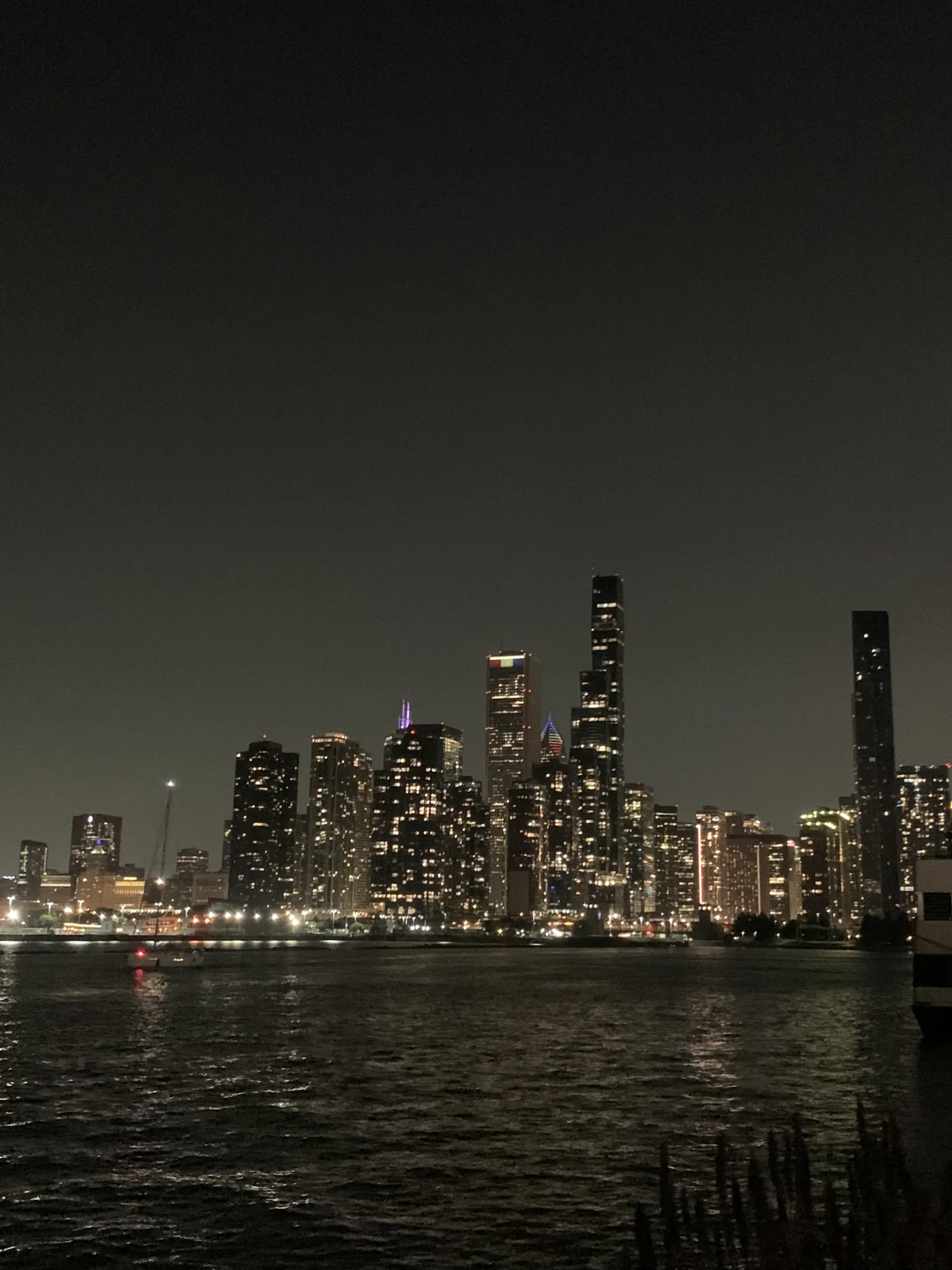 The Chicago skyline at night seen across dark water, with lit windows reflecting on the lake